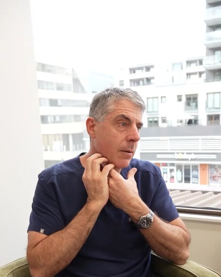 Dr. Buonassisi in scrubs, touching his jawline as he explains a facelift