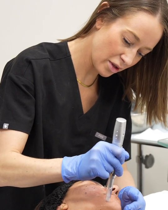 A medical aesthetician using a microneedling pen in a treatment room