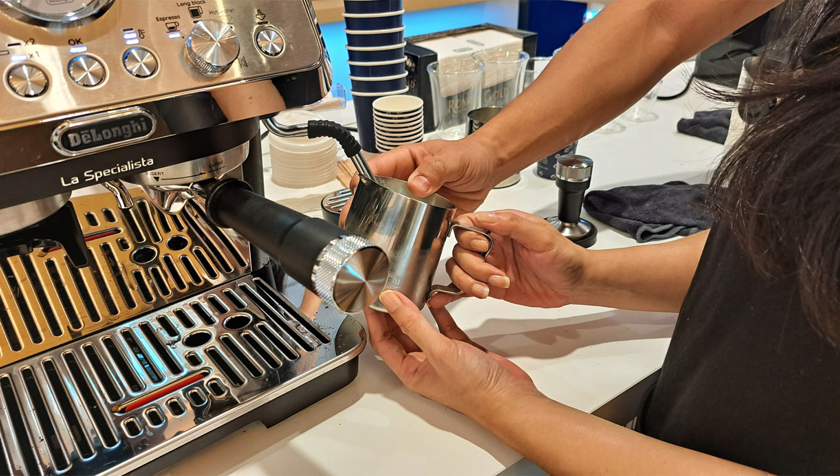 A brand ambassador assisting someone with frothing the hot milk using the coffee machine's steaming wand