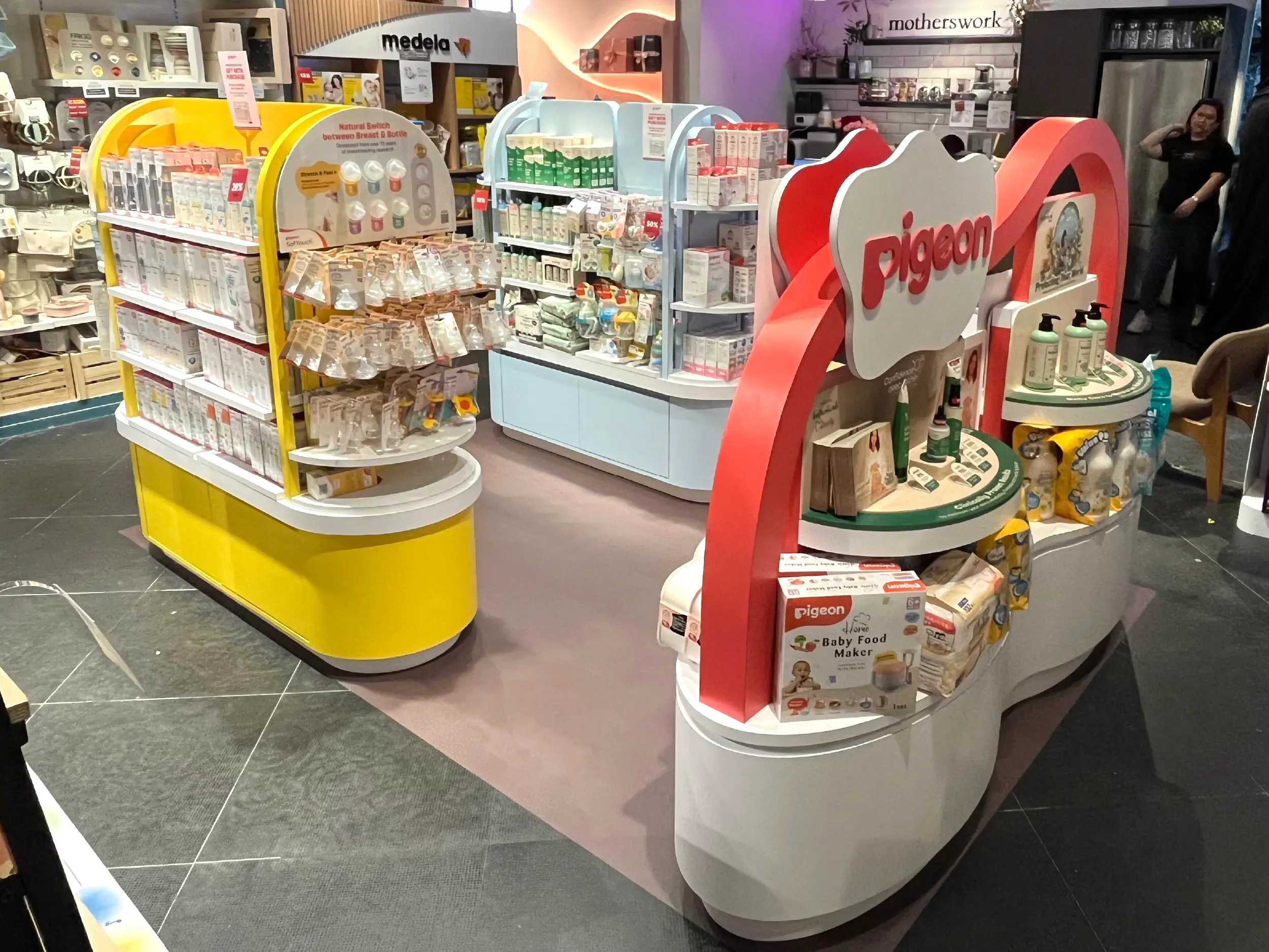 Retail display of baby care products including bottles, baby food maker, and lotions from brands Pigeon inside a store.