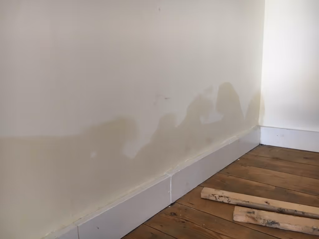 A wall with visible water stains near the floor, next to two wooden planks.
