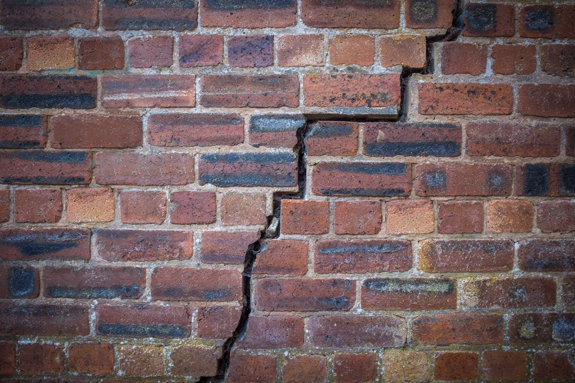 A brick wall with a large, uneven crack running vertically through it.