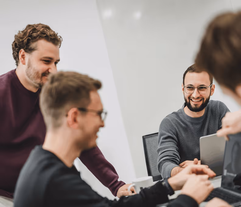 4 team members smiling while sitting infront of laptops coworking