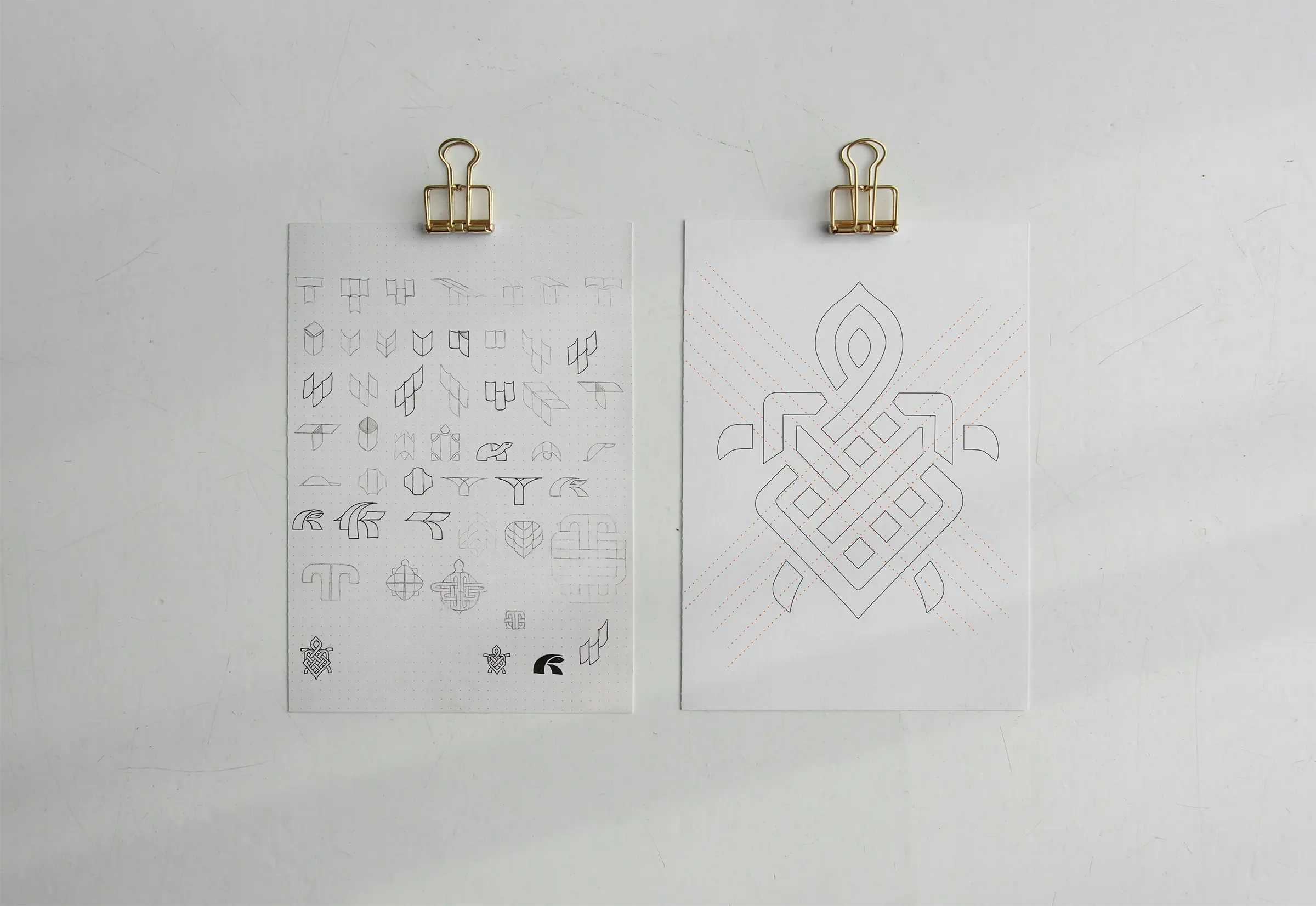 Two pieces of paper hung on a white wall, the one on the right shows the initial rough sketches for the Testudo branding project. On the right is the chosen mark which looks like a mix of a turtle and a celtic knot, shown in outlines.