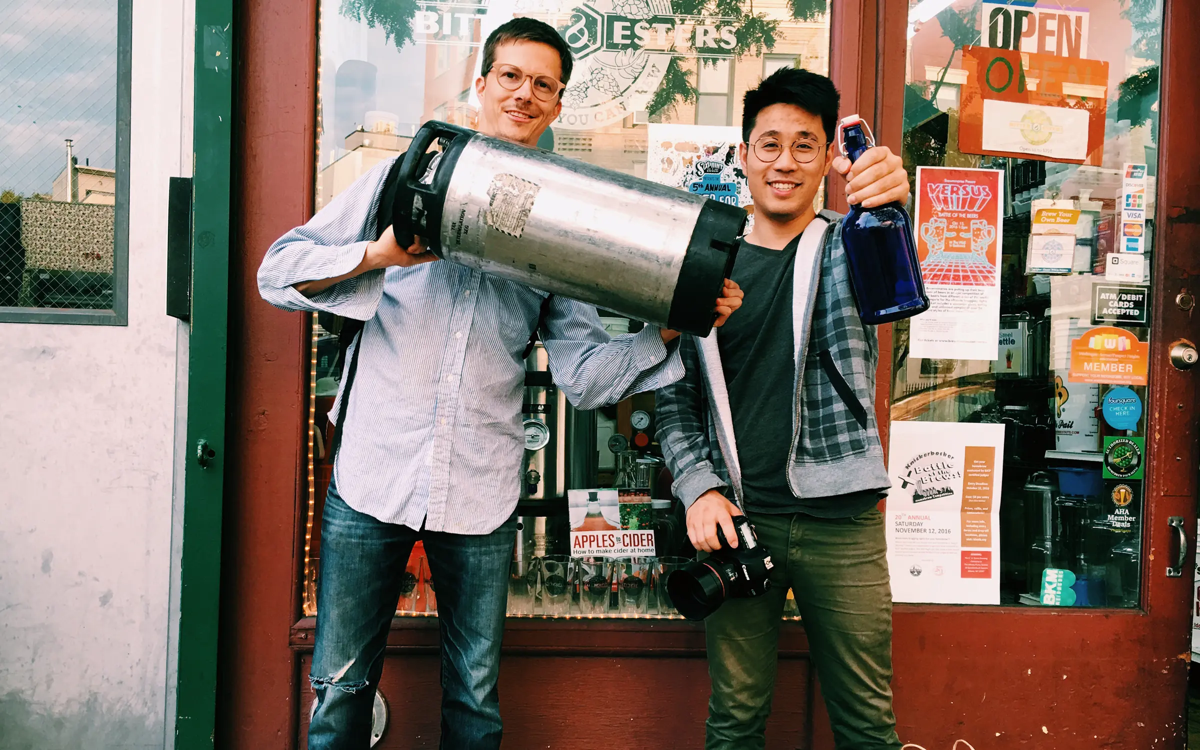 Brent Lagerman and Thi Lam in front of Bitters & Esters showing off a keg and a bottle for making Keepers.