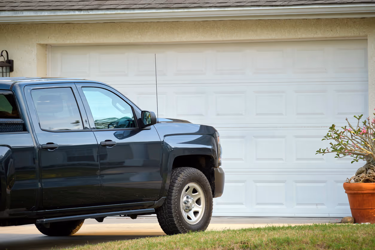 Car parked in front of wide garage double door on concrete driveway - home and auto insurance bundling concept