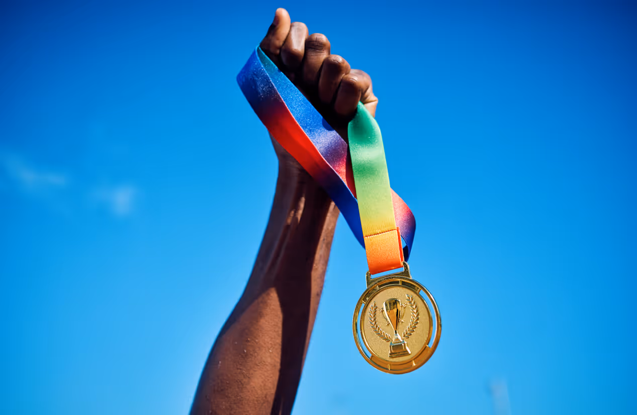 Raised hand holding a gold medal against blue sky. Best of the best concept