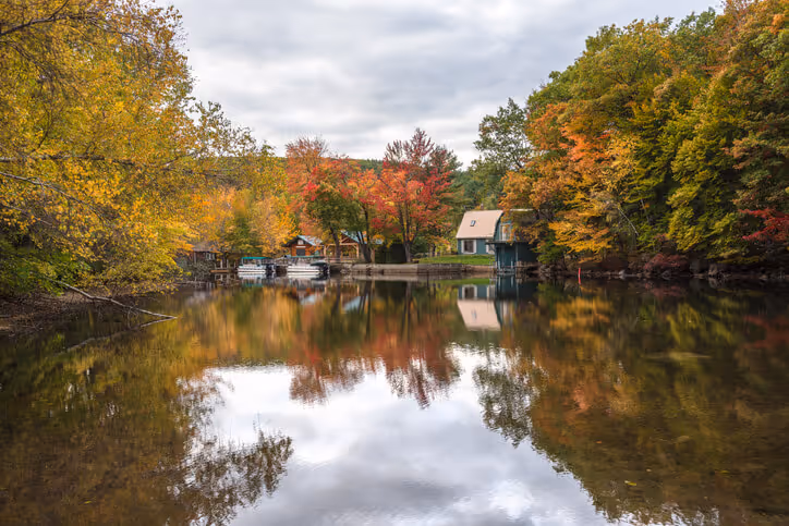 new hampshire homeowners insurance concept - Boathouses and boats along a river with forested banks on a cloudy autumn day. Stunning autumn colours and reflection in water
