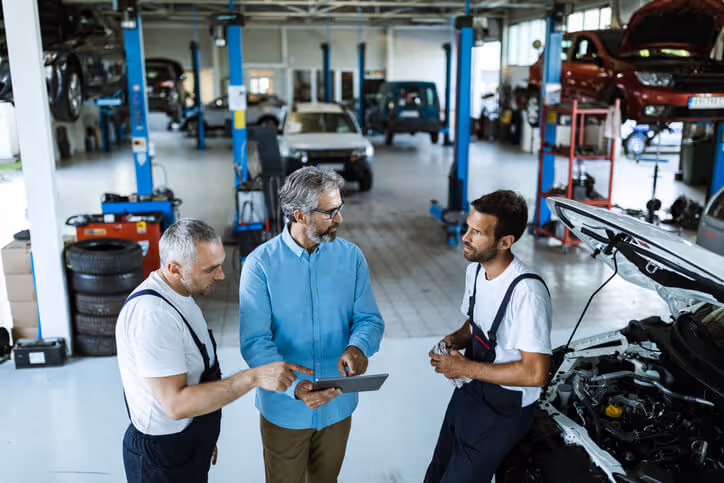 Mid adult manager using touchpad and talking to car mechanics in a workshop