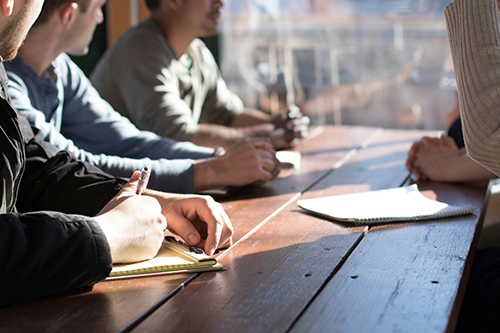 Group of people sitting at table talking with notepads