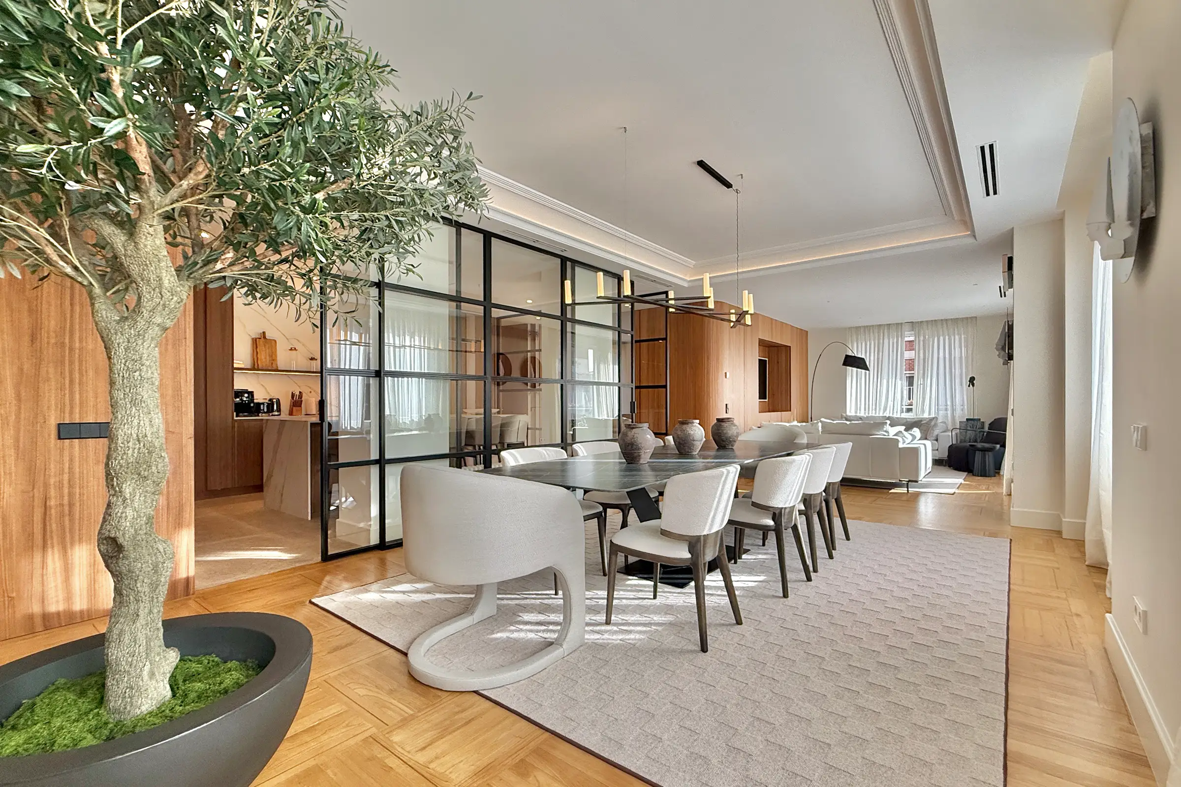 Concrete pathway flanked by green grass, small trees, curved stone walls, street lamps, and a modern white building under blue sky.