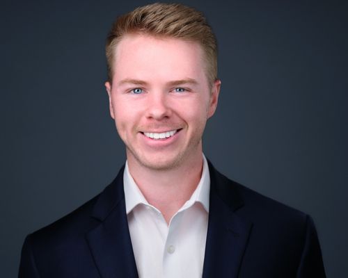 Josh Christner, professional headshot. A white man with combed back brown hair with a wide smile on his face. He is wearing a suit jacked and collared shirt.