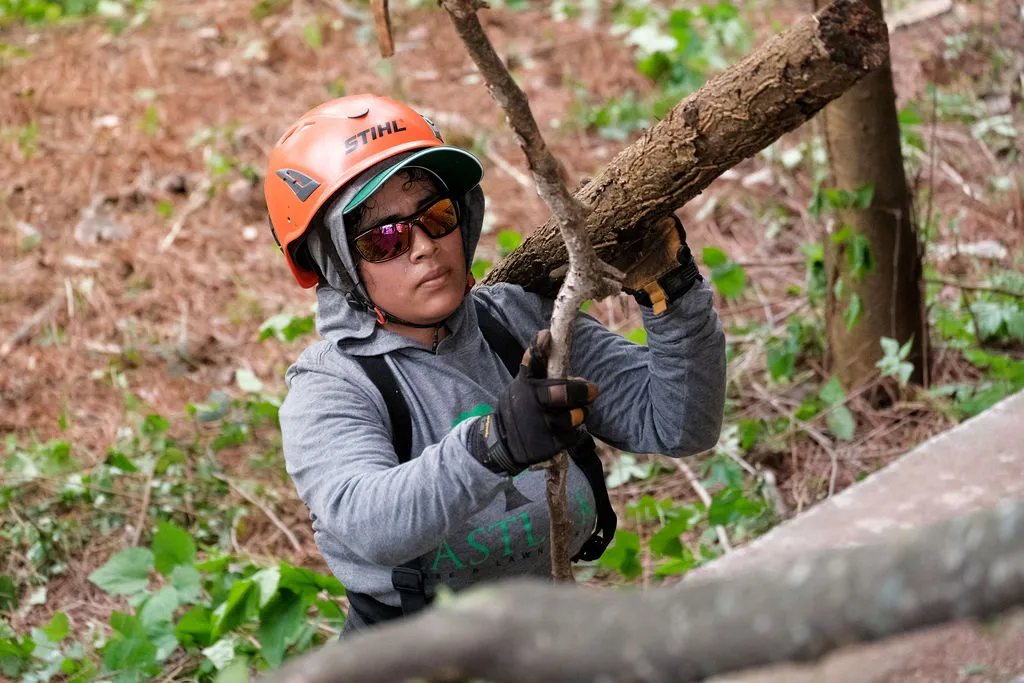 Person wearing an orange helmet and sunglasses carrying a large tree branch in a forested area. Professional arborist from EastLake Tree Services working on Atlanta property.