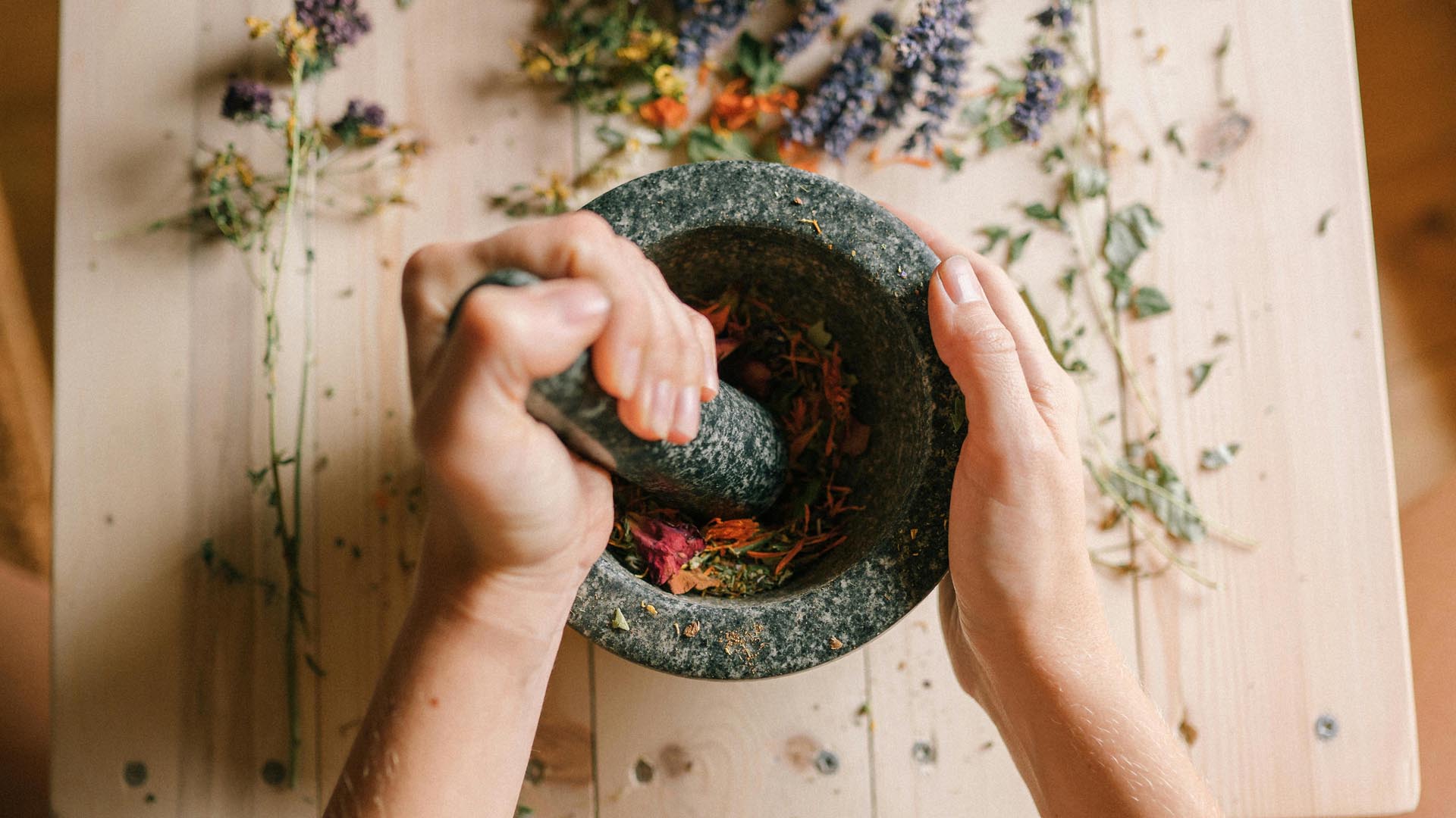A woman pounding dried herbs and flowers in a mortar and pestle.