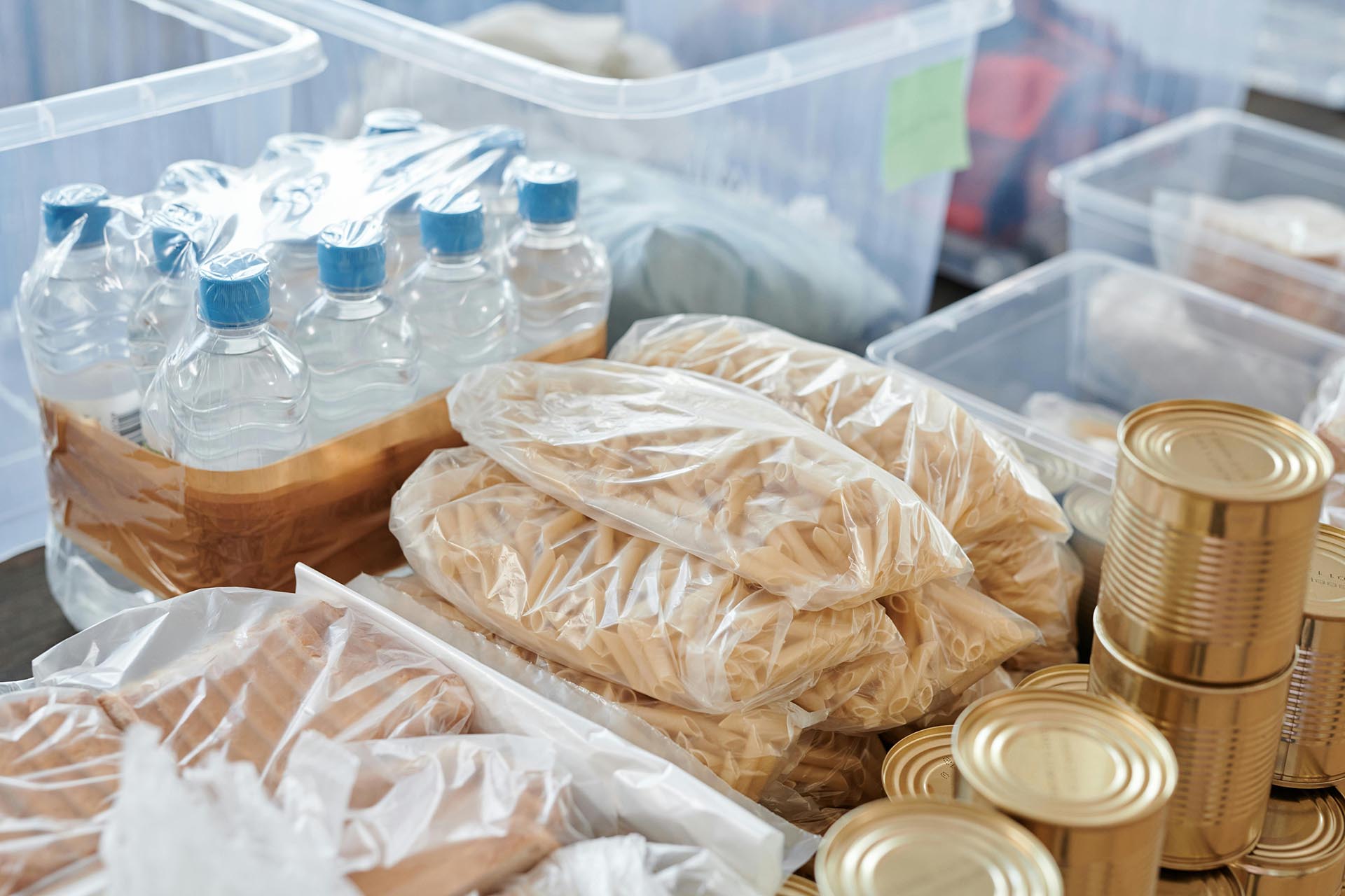 A photo of water bottles, pasta, and canned food in tubs.