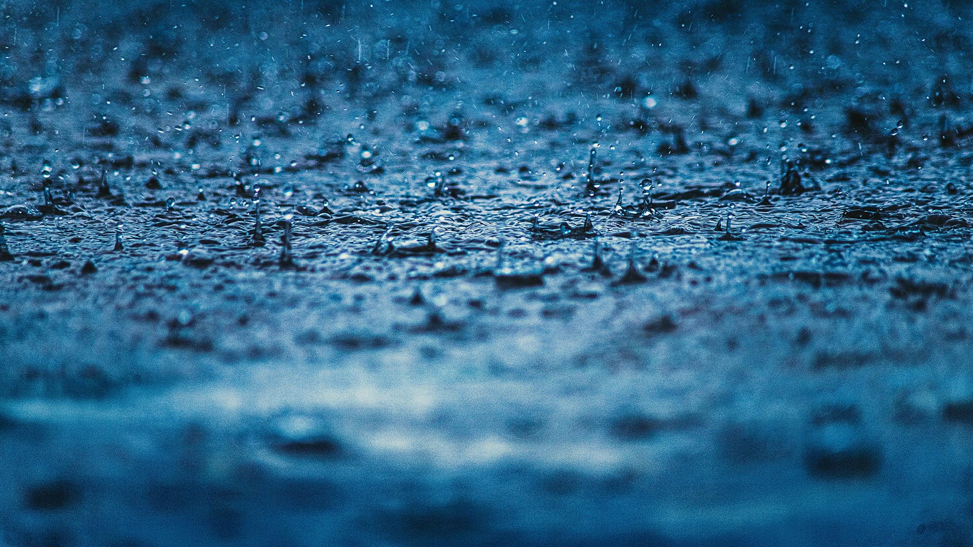 A photo of raindrops falling in blue water.