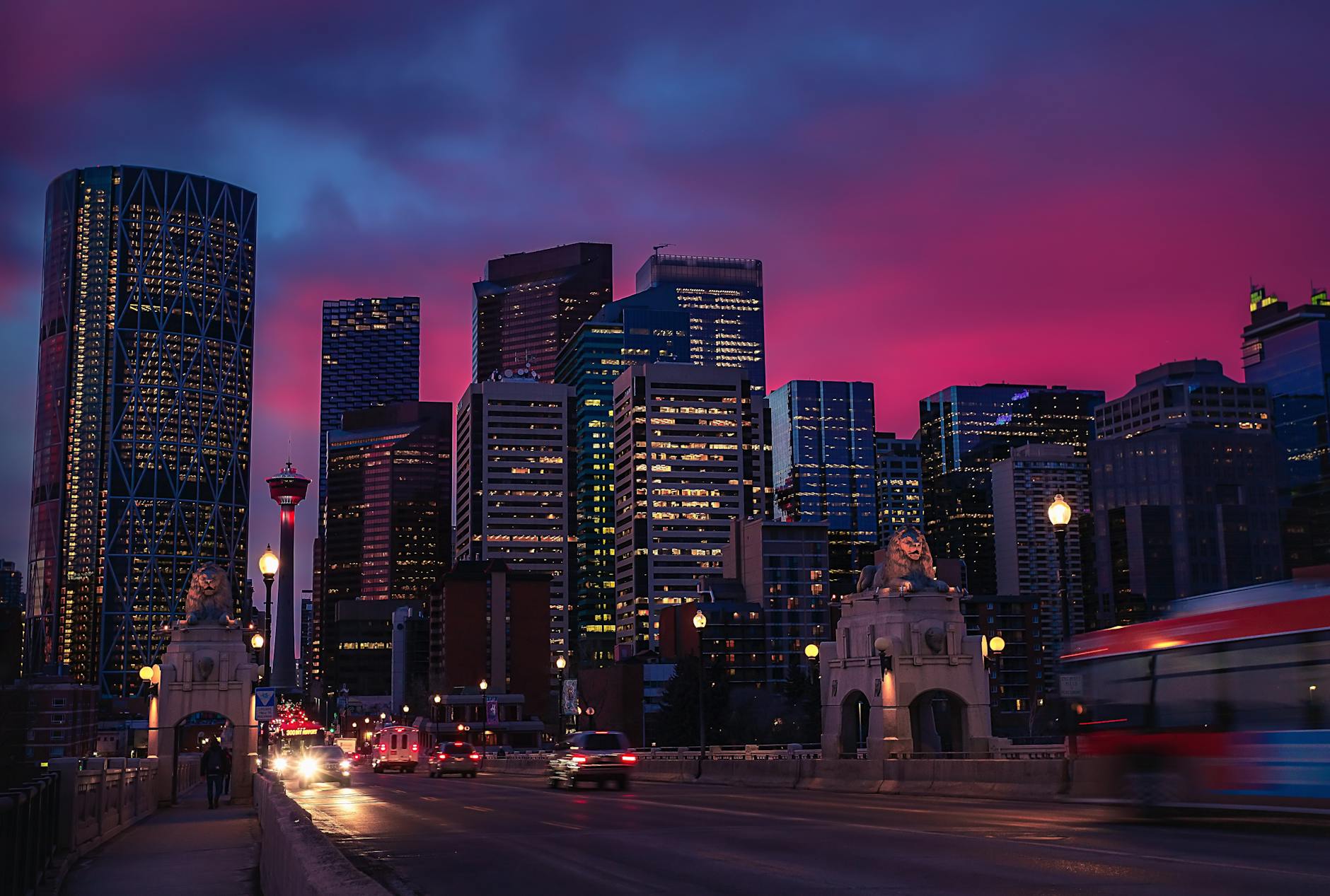 Stunning view of Calgary's illuminated skyline during a vibrant pink sunset, featuring skyscrapers and urban landscape.