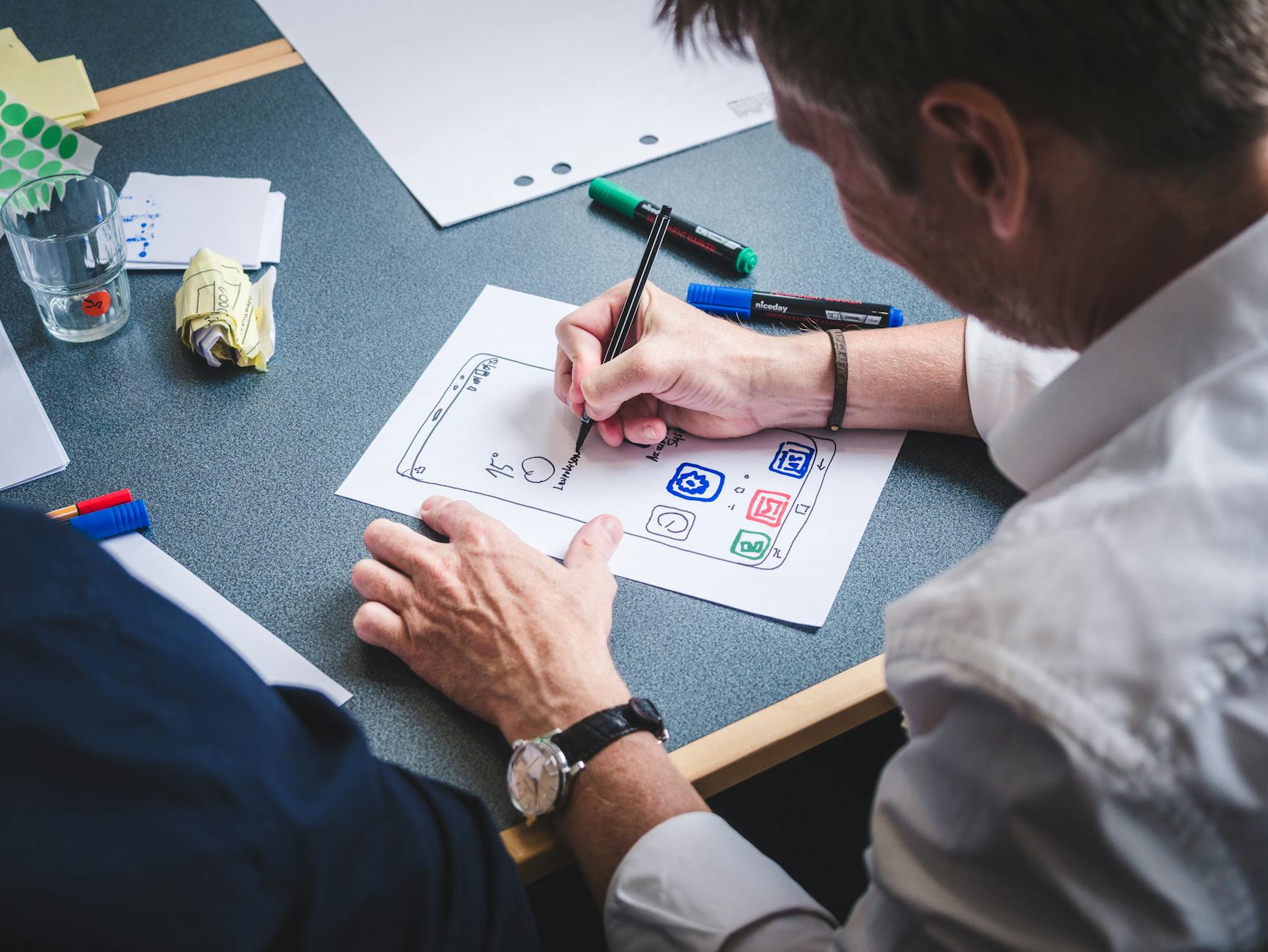 A designer sketches a mobile app prototype on paper at an office desk, focusing on creativity and design.