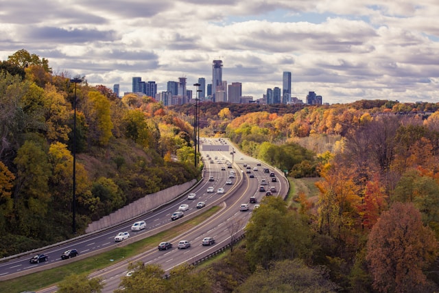 A highway winding through autumn trees toward a city skyline