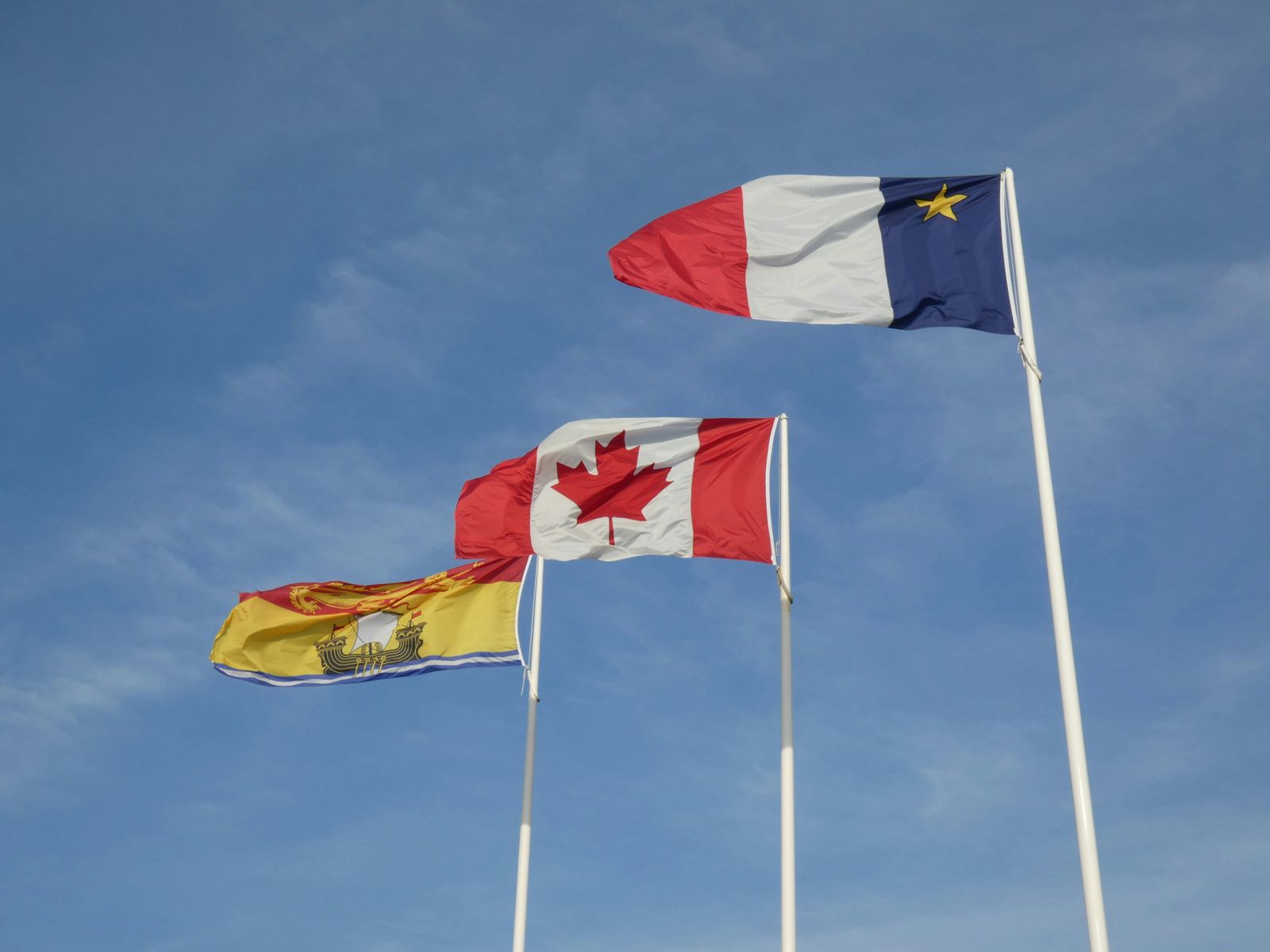 Acadian, Canadian and New Brunswick flags flying against a blue sky