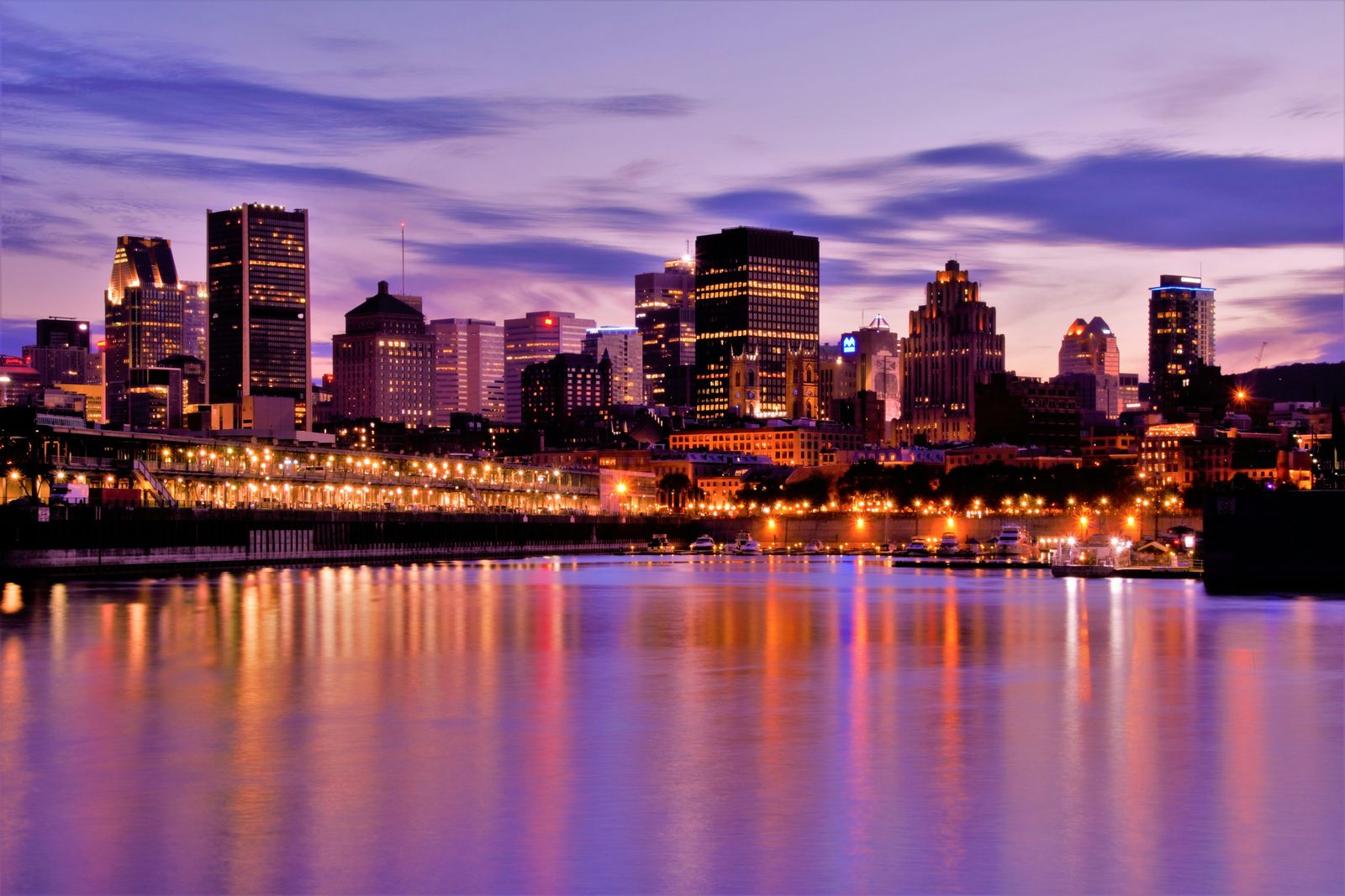 A city skyline lit up at dusk and reflected in the water