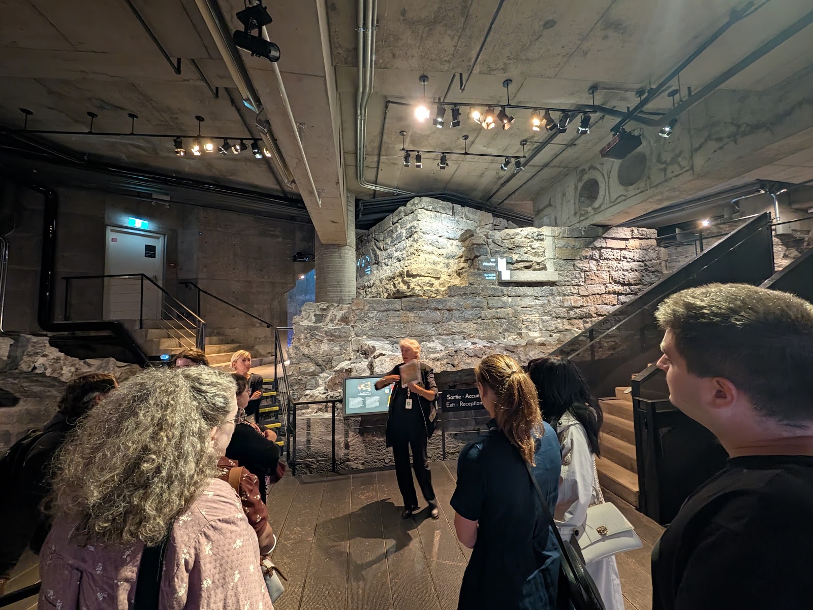 A guide speaks to visitors beside stone foundations preserved beneath Pointe-à-Callière museum in Old Montreal
