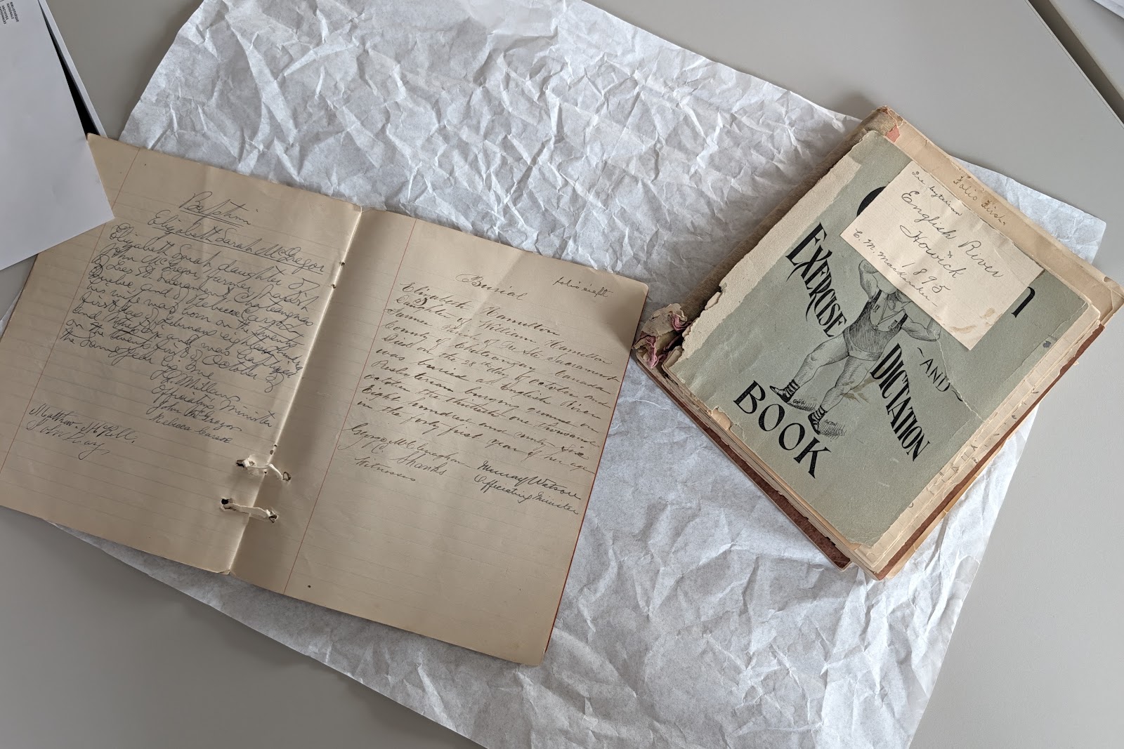 A handwritten notebook and a vintage dictation exercise book laid out on archival tissue