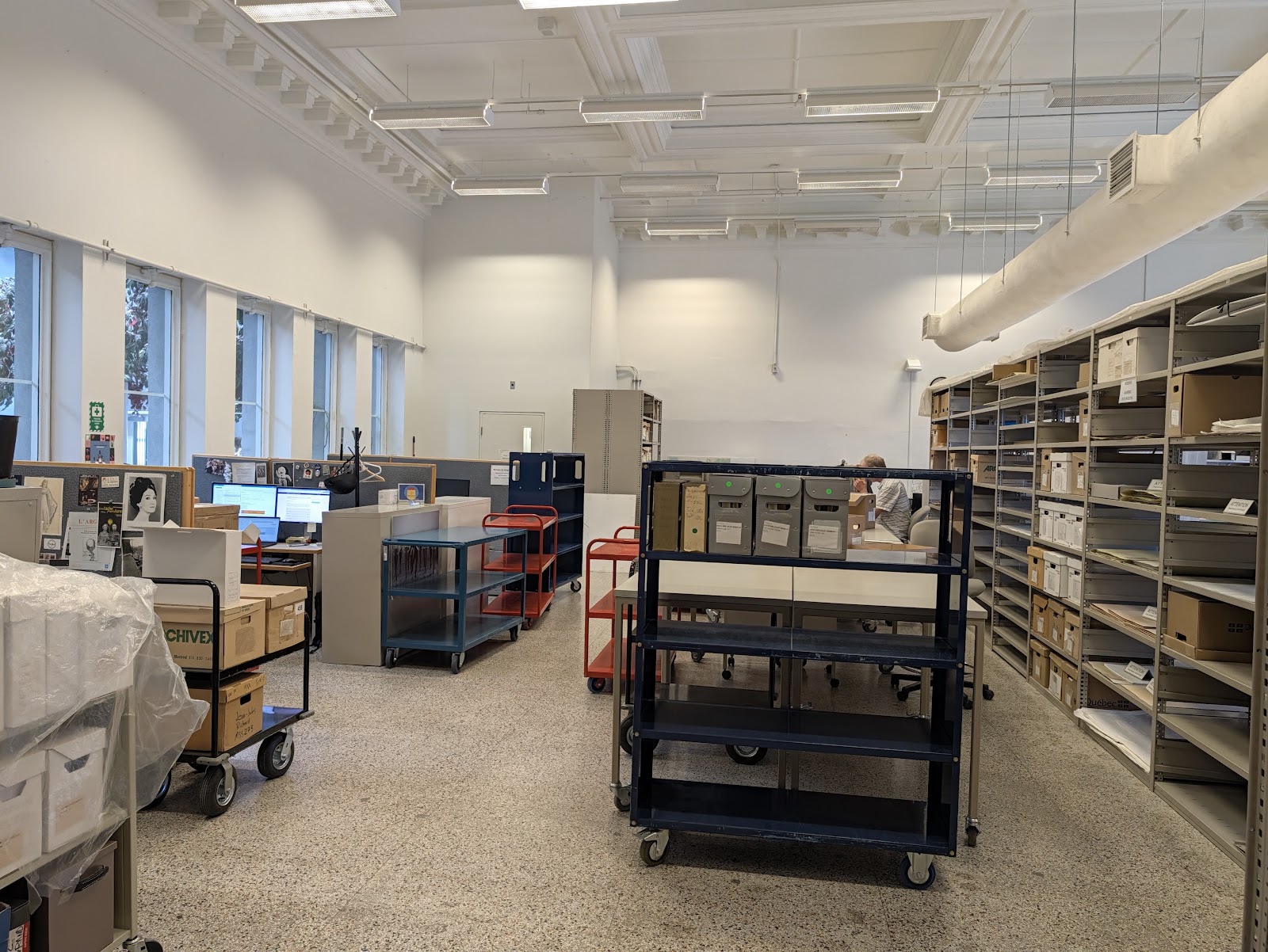 The BAnQ workroom where staff retrieve registers and prepare certified copies, with carts, archival boxes and shelving