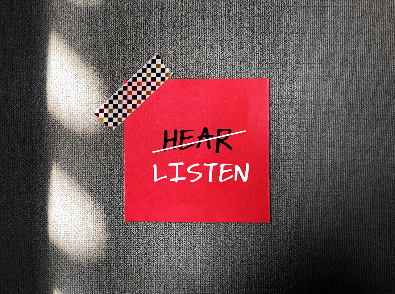 Ein Post-IT auf dem "Hear" (Hören) durchgestrichen ist und darunter "Listen" (Zuhören) steht