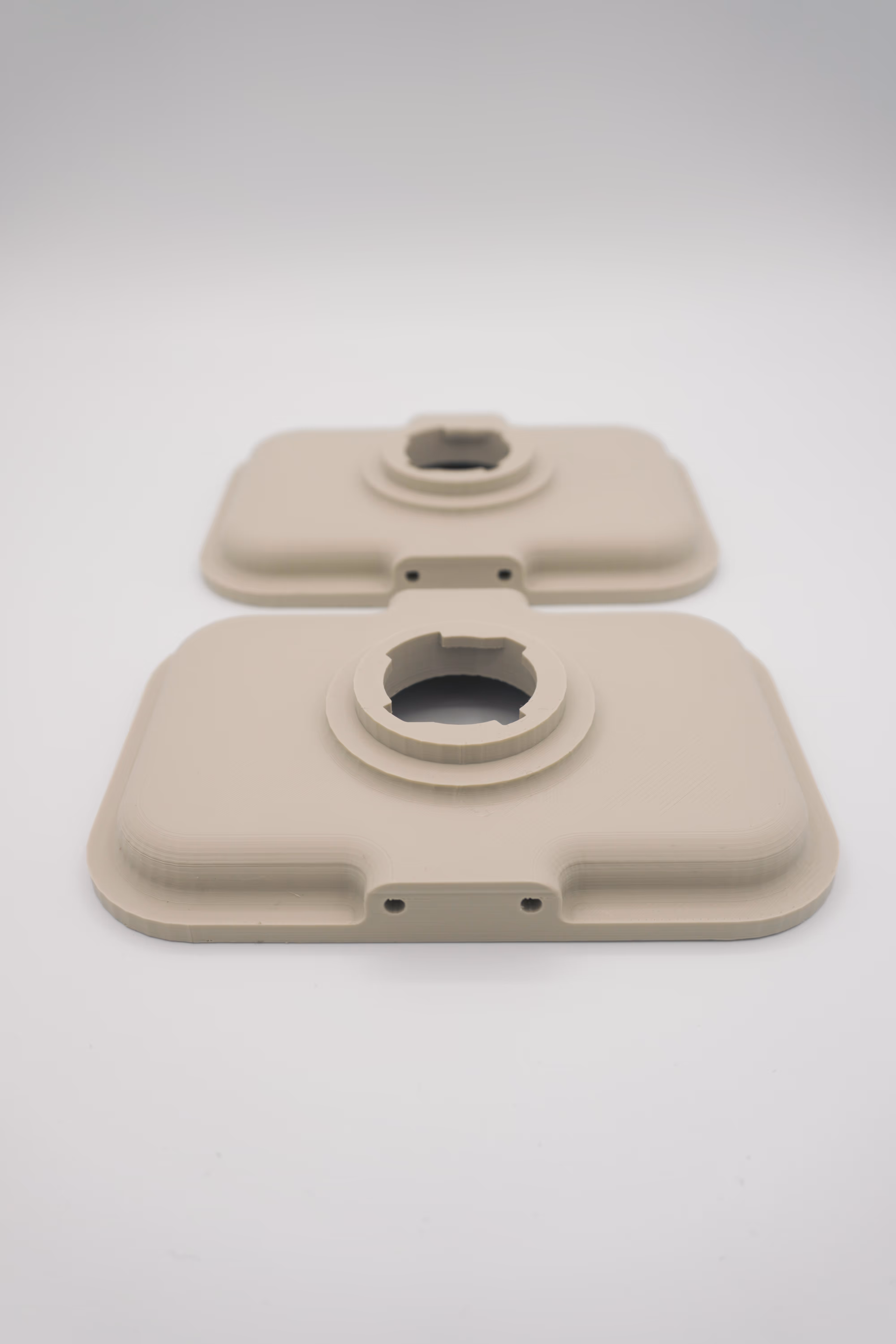 Twee beige 3D-prints van rechthoekige panelen met afgeronde hoeken, een centraal rond bevestigingselement en twee montagegaten