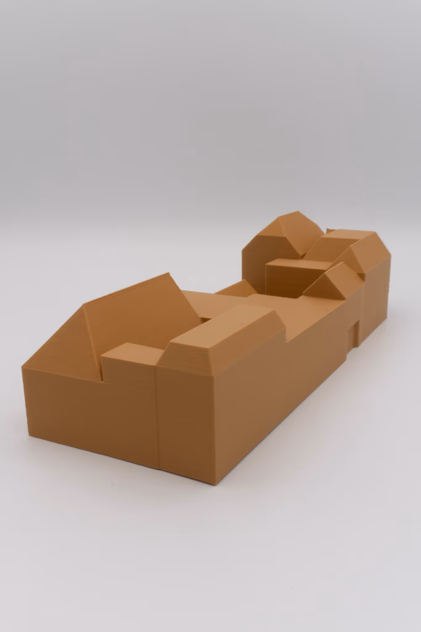 Bruin 3D-geprint gebouwmodel met schuine daken op witte achtergrond