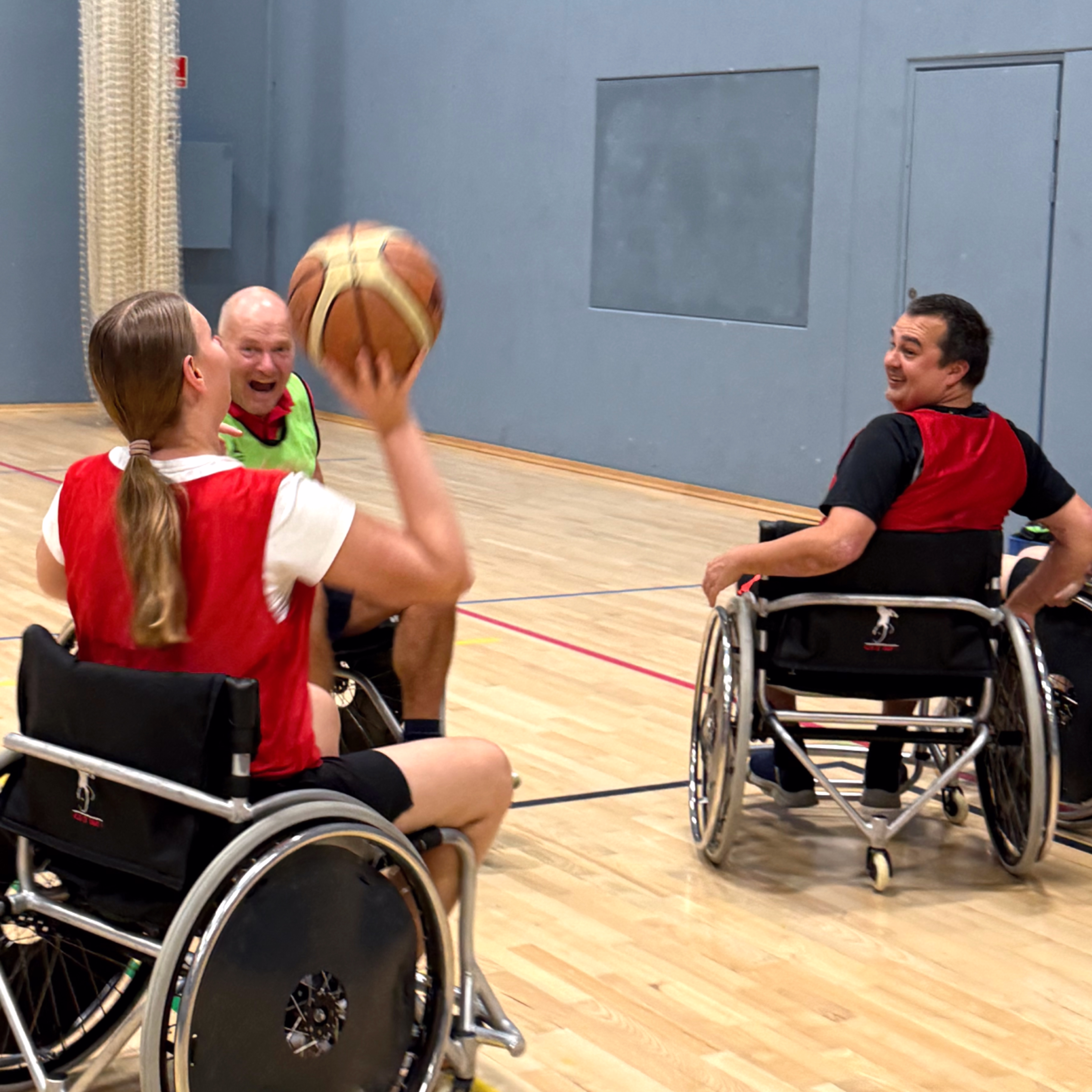 3 spillere i kørestolsbasket. En spiller aflevere mod en anden mens modstander er klar til angreb