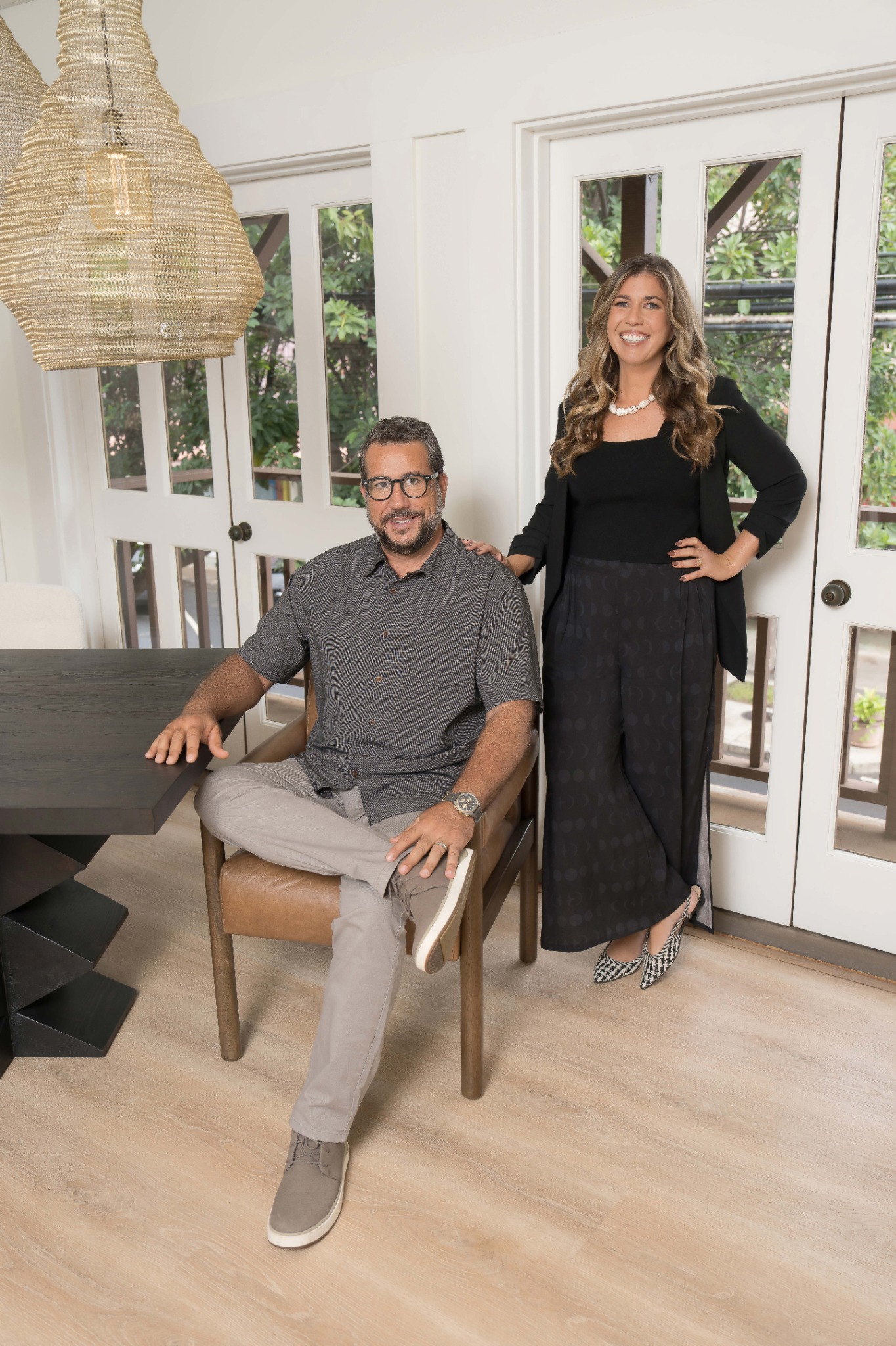 Martin Gastaldi sitting on a chair with Stefanie Gastaldi standing beside him in Patina Studio a bright room with glass doors and wooden floor.