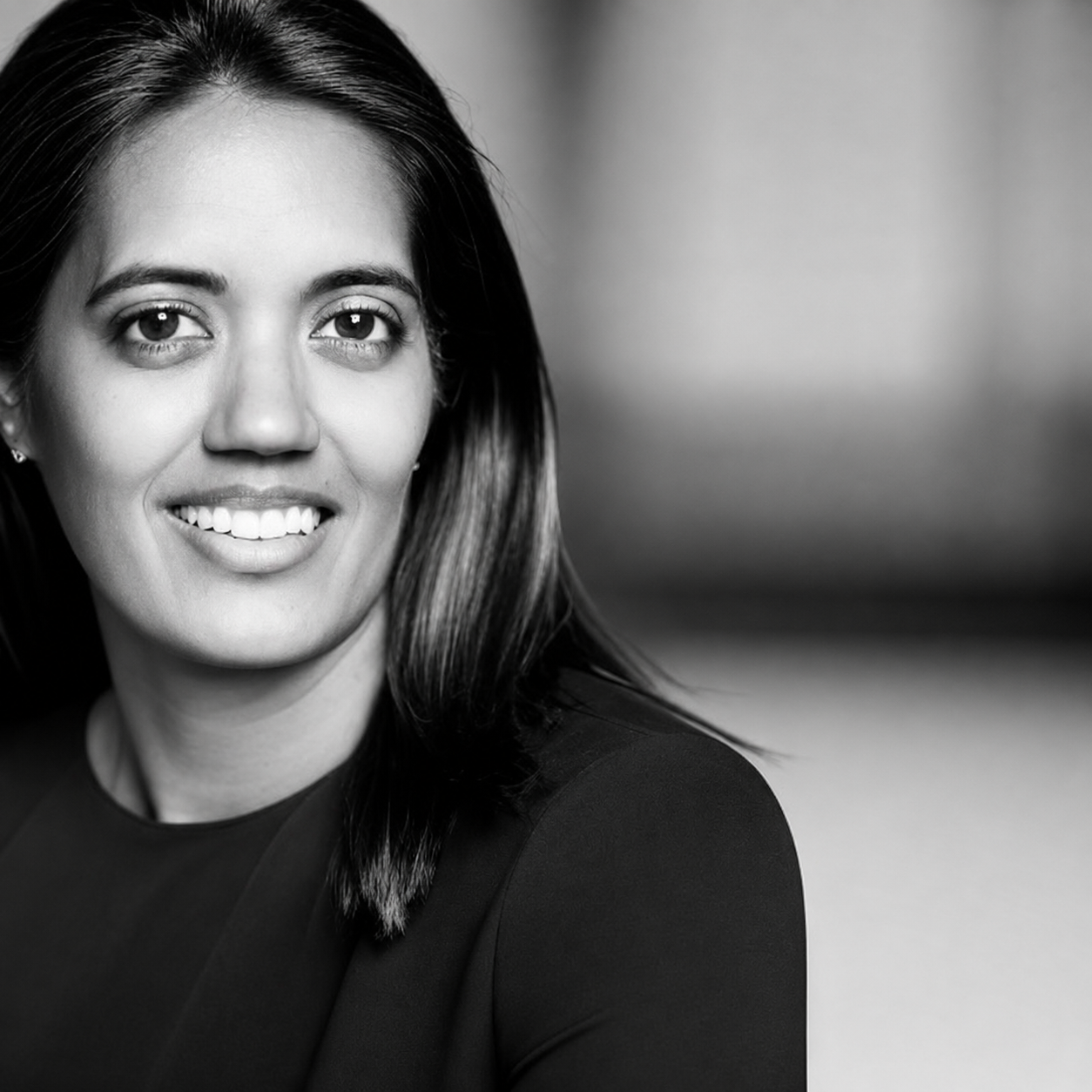 Black and white portrait of a smiling woman with straight hair wearing a dark top.