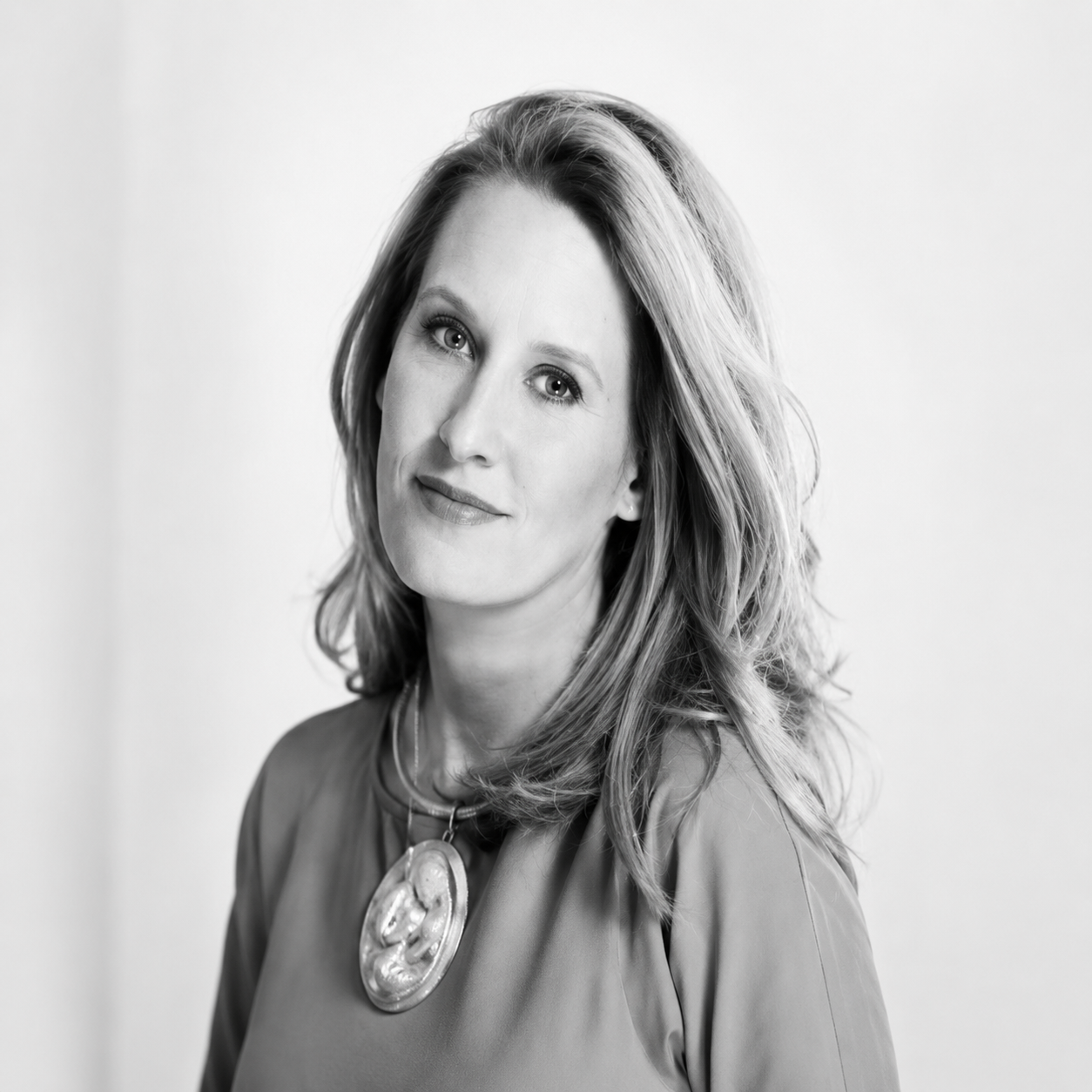 Black and white portrait of a woman with light hair wearing a round pendant necklace and a calm expression.