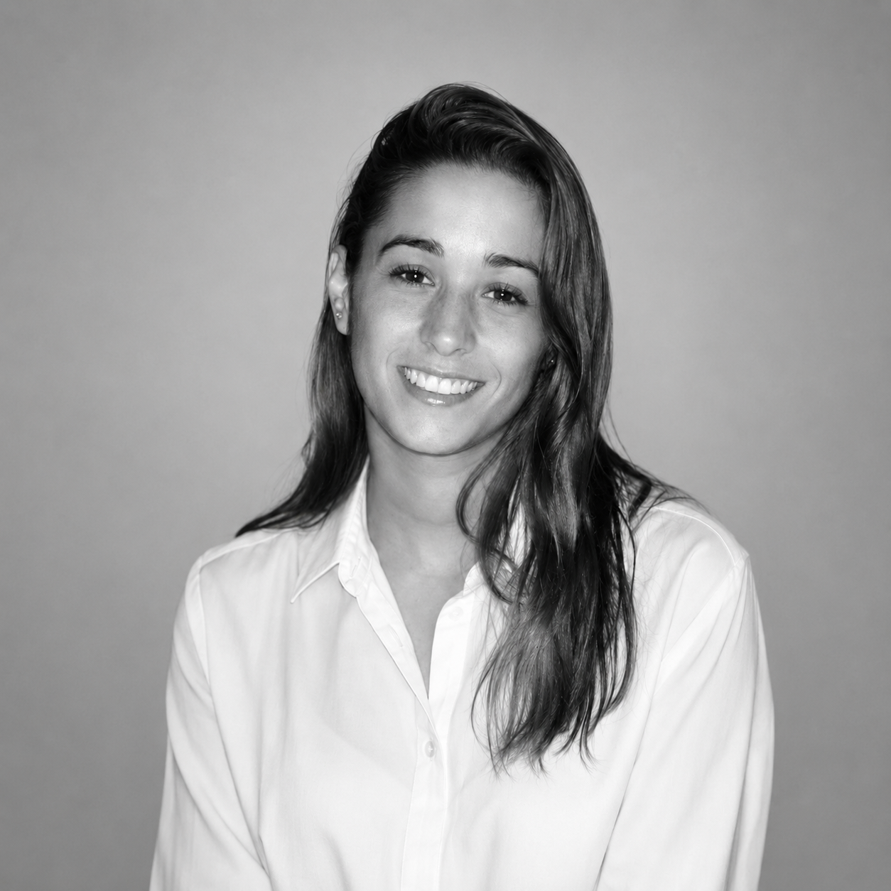 Smiling woman with long hair wearing a white button-up shirt against a plain background.