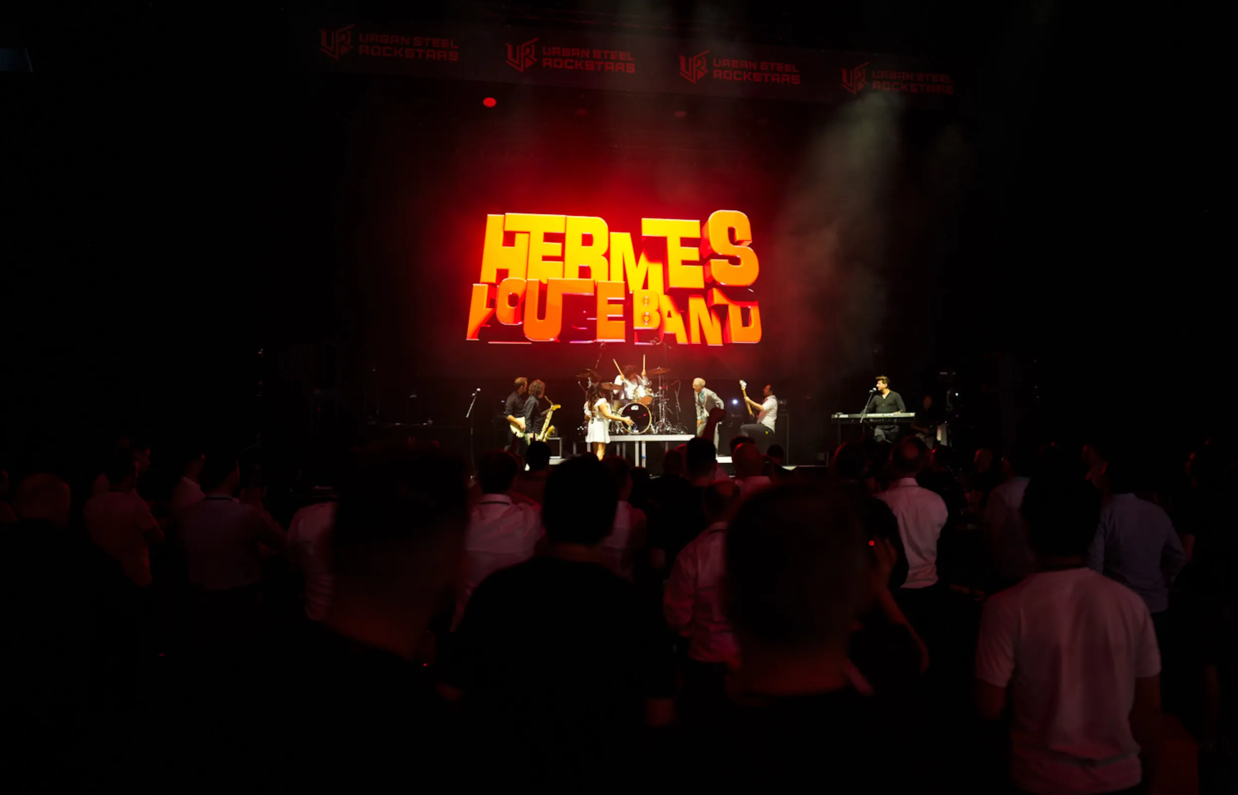 Live-Bühne mit großem roten Schriftzug „Hermes House Band“, Zuschauer vor der Stage.