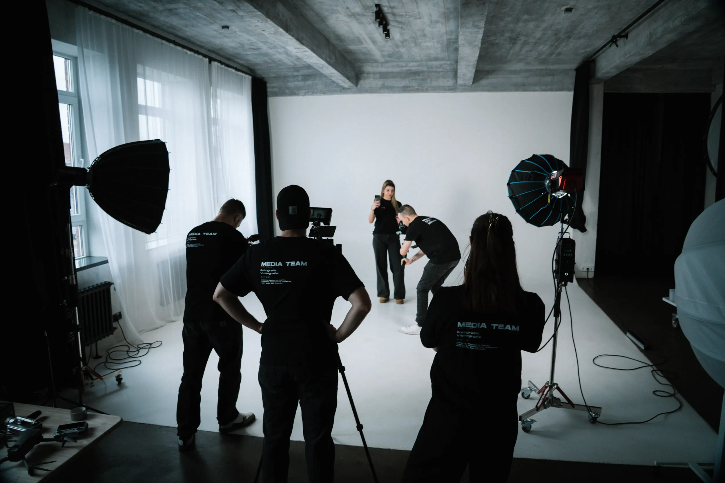 Videodreh im Fotostudio: Kameracrew richtet Licht und Kamera vor weißem Hintergrund ein.