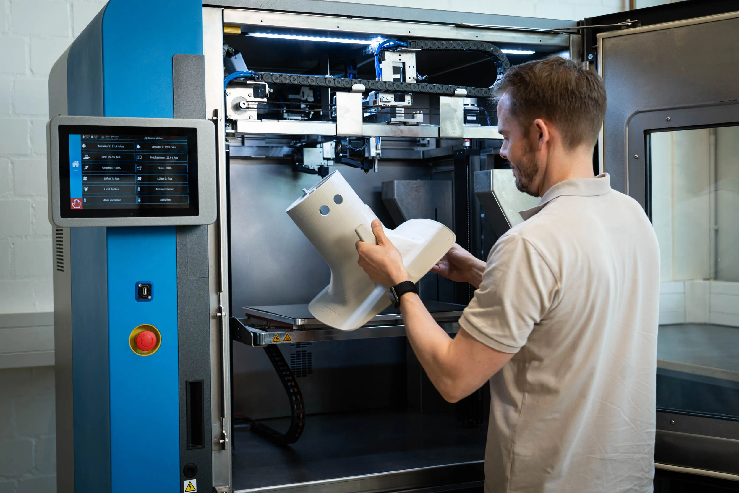 Mitarbeiter entnimmt großformatiges 3D-Druck-Bauteil aus industriellem Drucker.