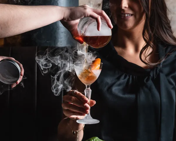 Serving smokey cocktails into female customer's hand
