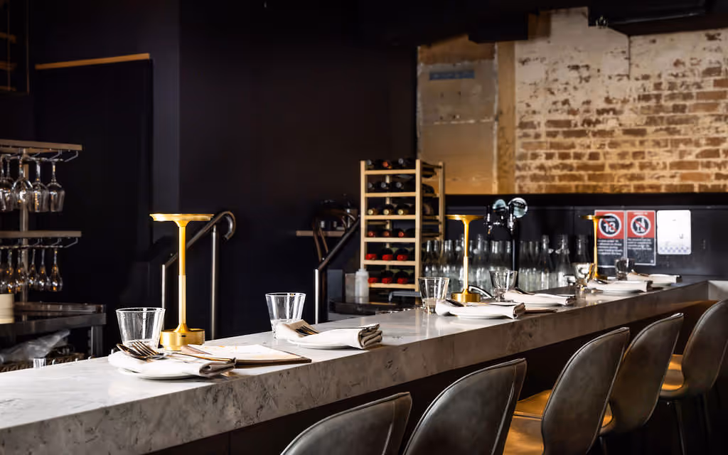 Marble bar with wine racks, glassware and gold lamps at Hustlers Sydney, highlighting premium beverage service for events.