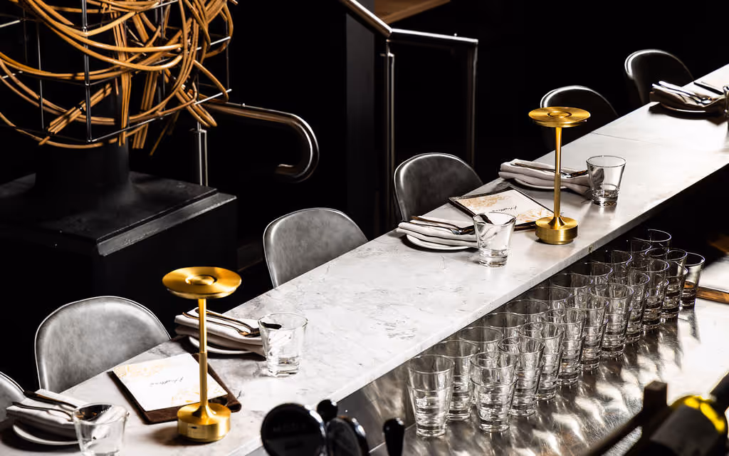 Long white-marble communal table with gold lamps and rows of glasses set for group dining at Hustlers Sydney.