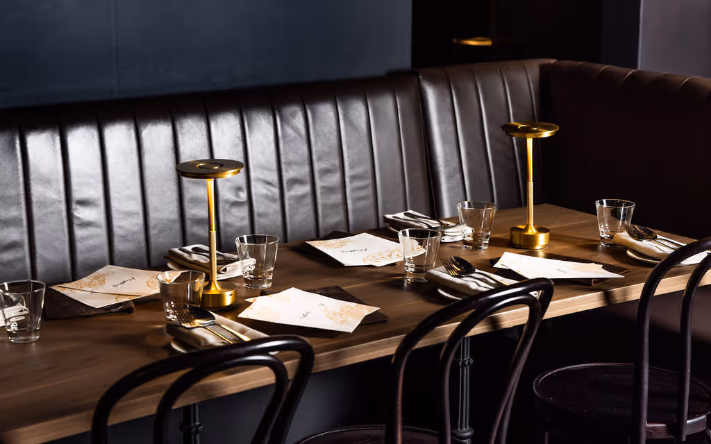 Close-up of stylish table setting, black leather banquette and gold lamp at Hustlers Sydney – perfect for intimate events.