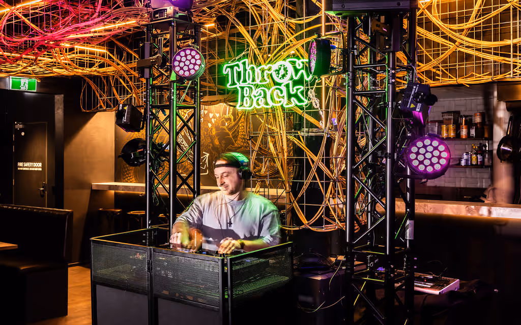 Resident DJ behind neon “Throwback” sign at Hustlers Sydney, signalling lively nightlife for party functions.