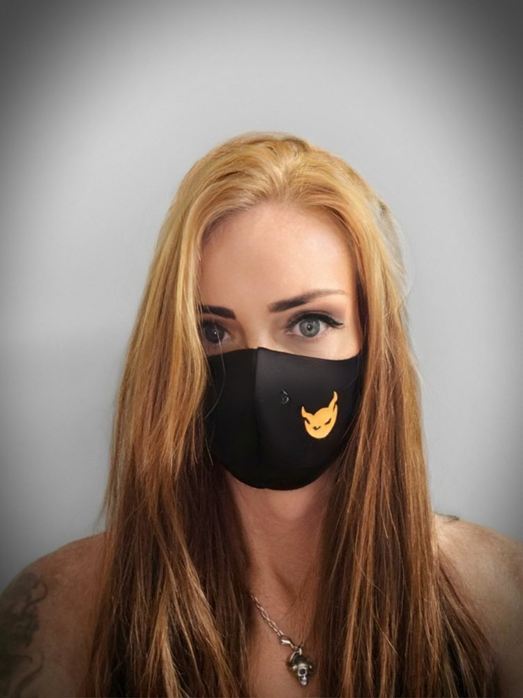 Johanna Browne with long strawberry blonde hair and a black face mask, against a grey background.