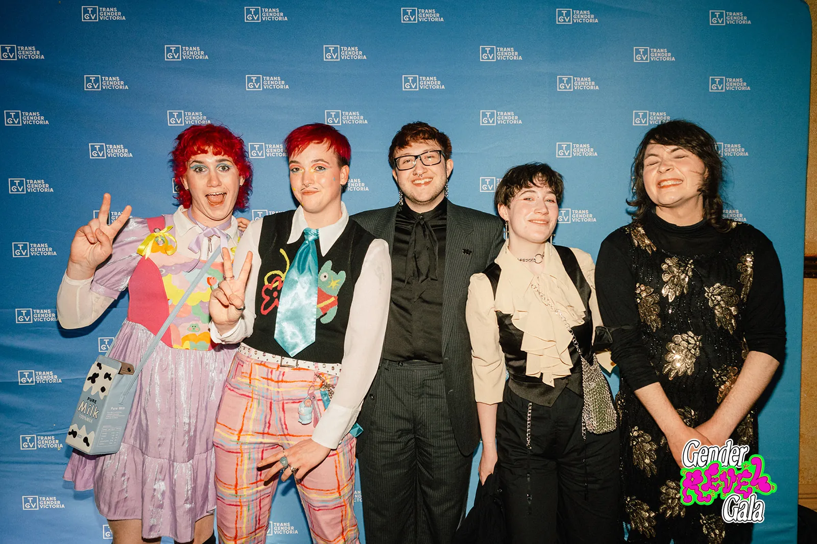 Five guests in colourful outfits smiling and posing on the red carpet at the Gender Revel Gala