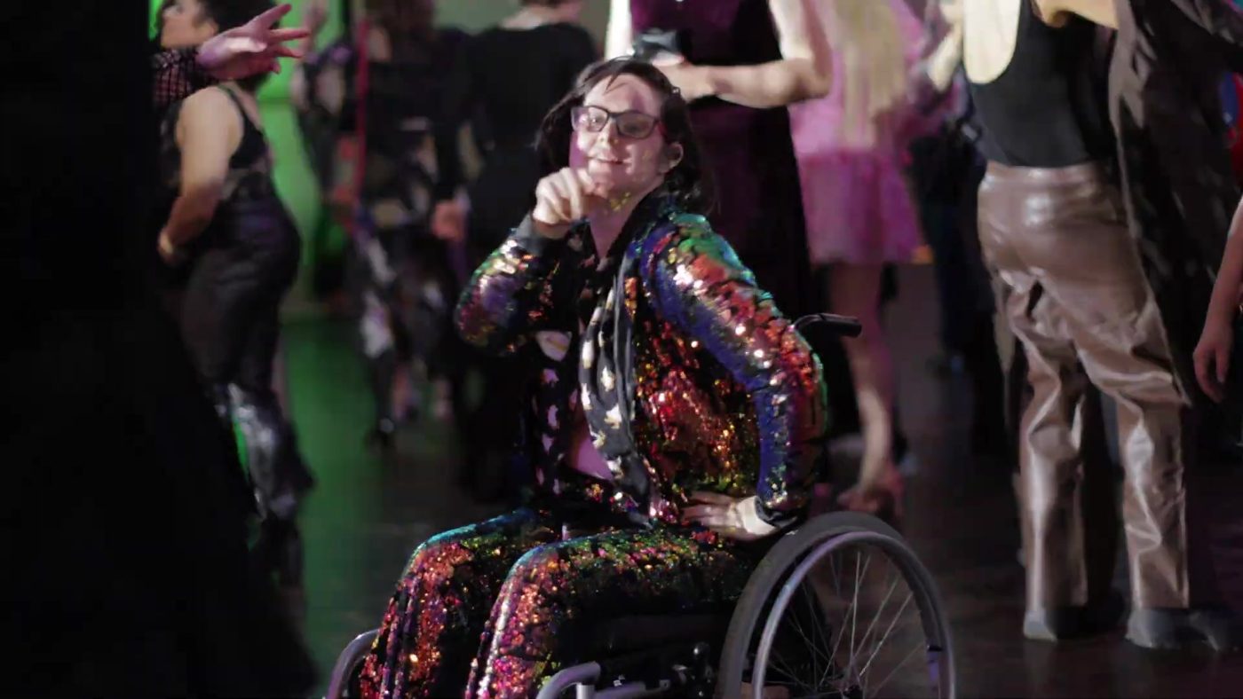 A guest in a rainbow sequin suit in a wheelchair on the dance floor at the 2025 Gala