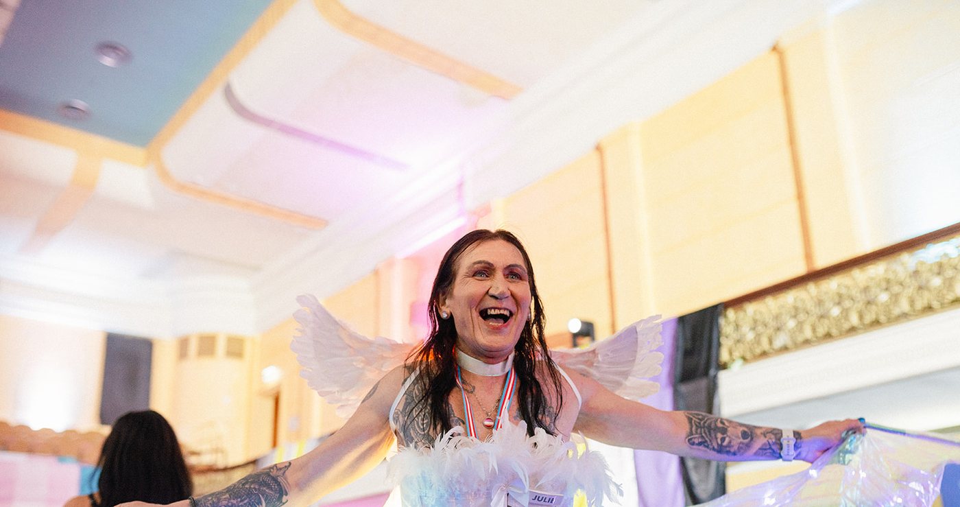 A guest in white feathered wings laughing on the dance floor