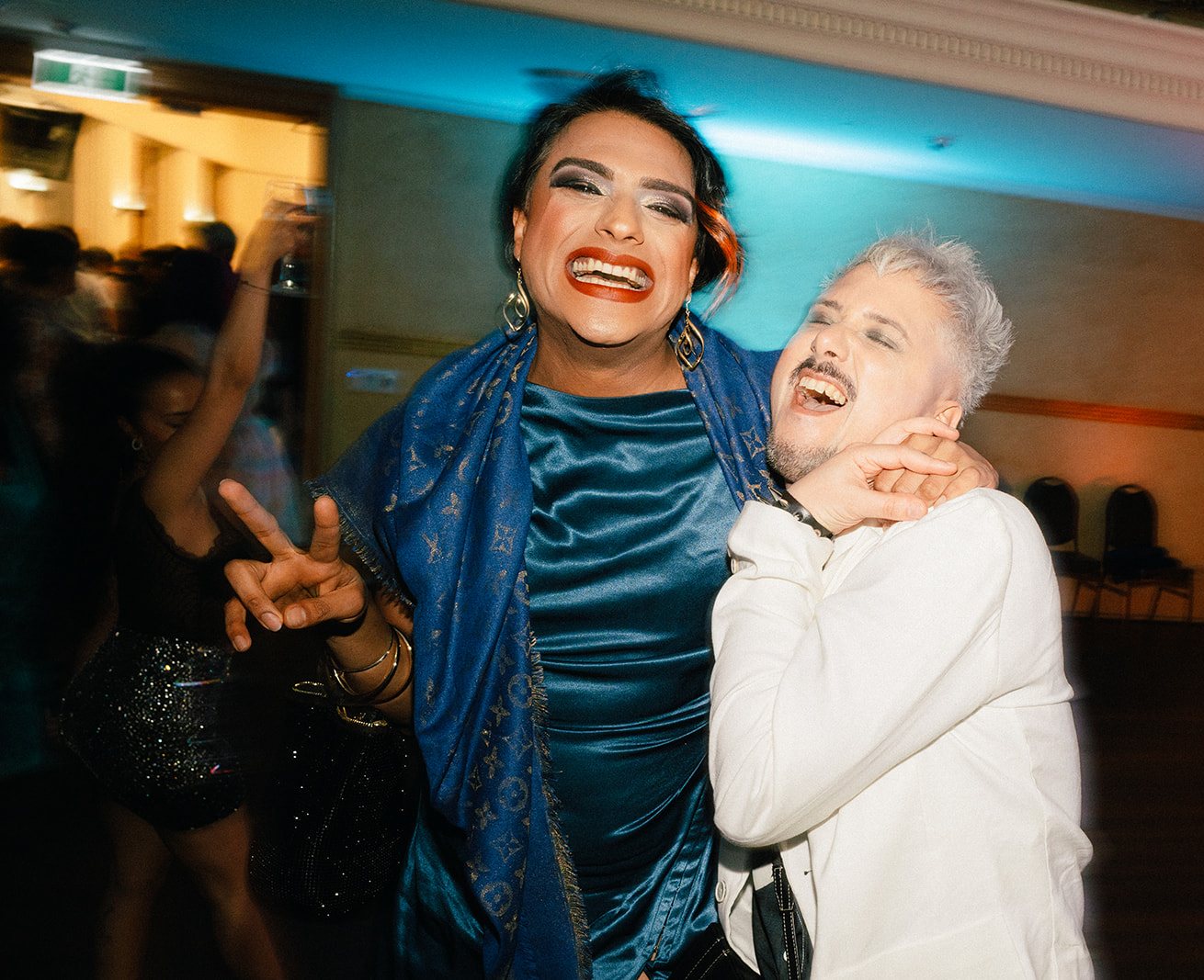 Two guests hugging and grinning on the dance floor, one in a blue velvet dress