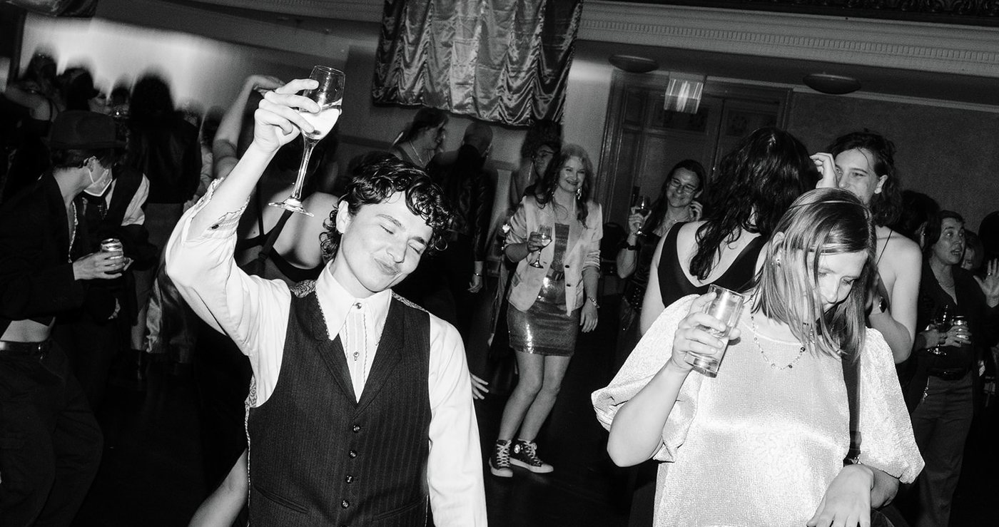 A black and white photo of guests dancing with their drinks in the air